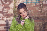 a woman in a green shirt leaning against a brick wall